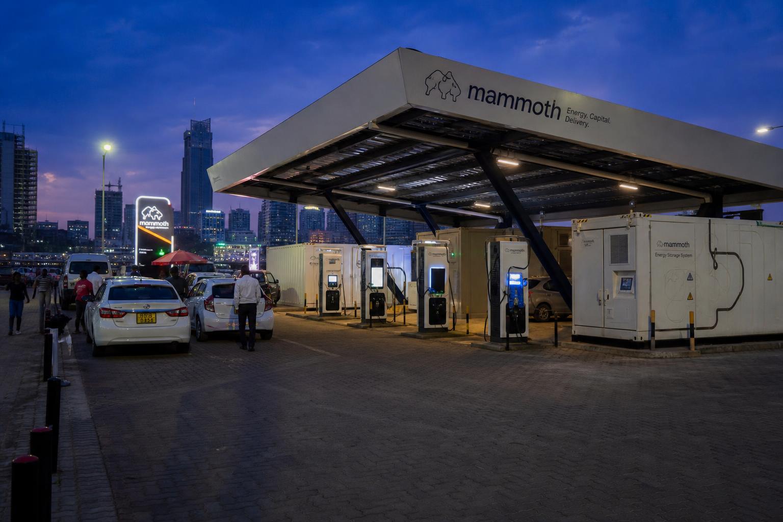 A GMF Mammoth Energy distributed energy node at dusk — solar canopy, battery containers and ultra-fast chargers in an African city